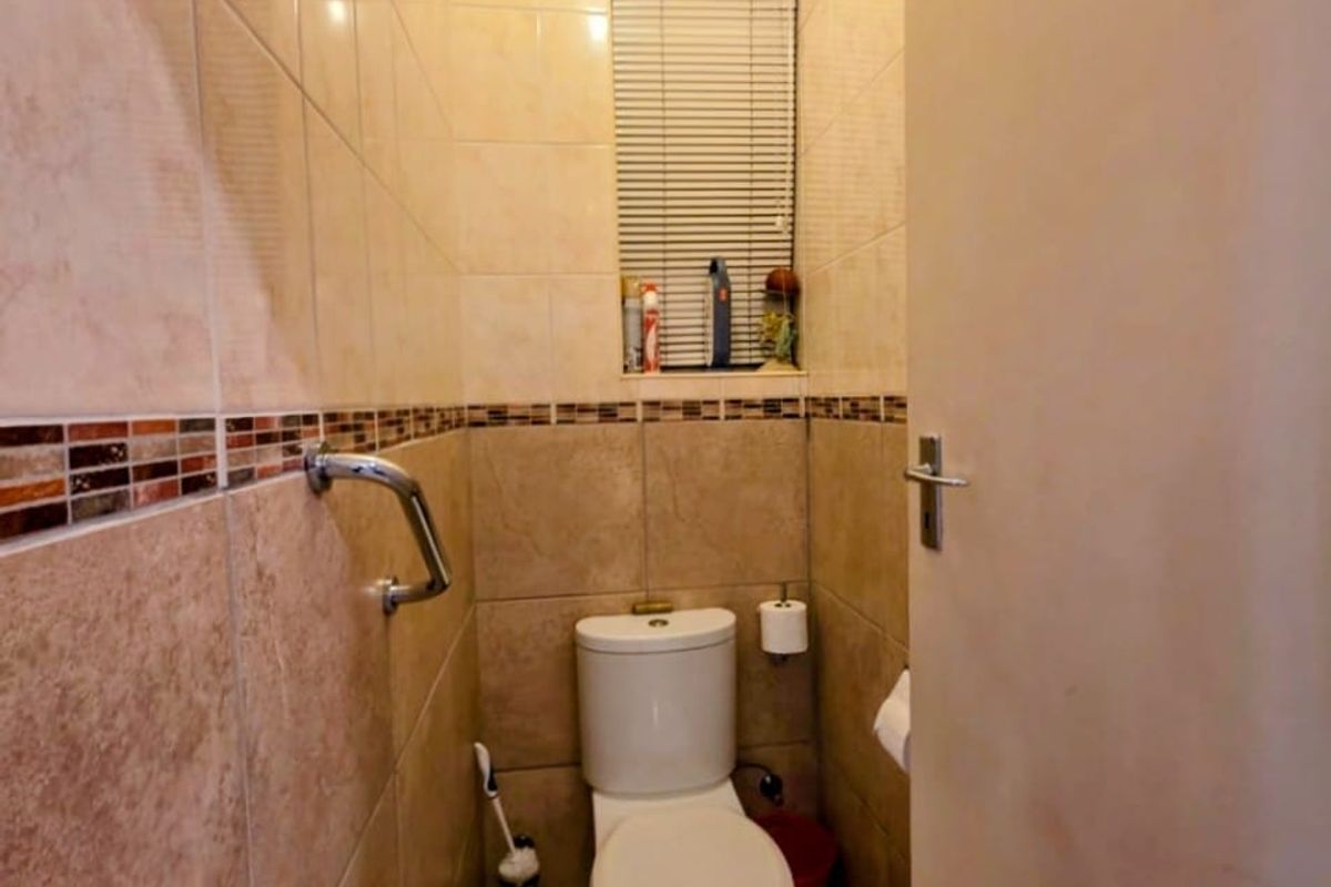 A compact bathroom featuring neutral ceramic wall and floor tiles, a standard toilet, and a functional grab rail for accessibility.