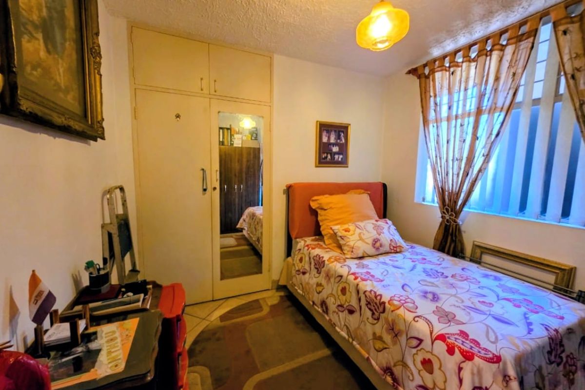 A functional bedroom featuring a built-in wardrobe with a mirrored panel and a ceiling pendant light fixture.