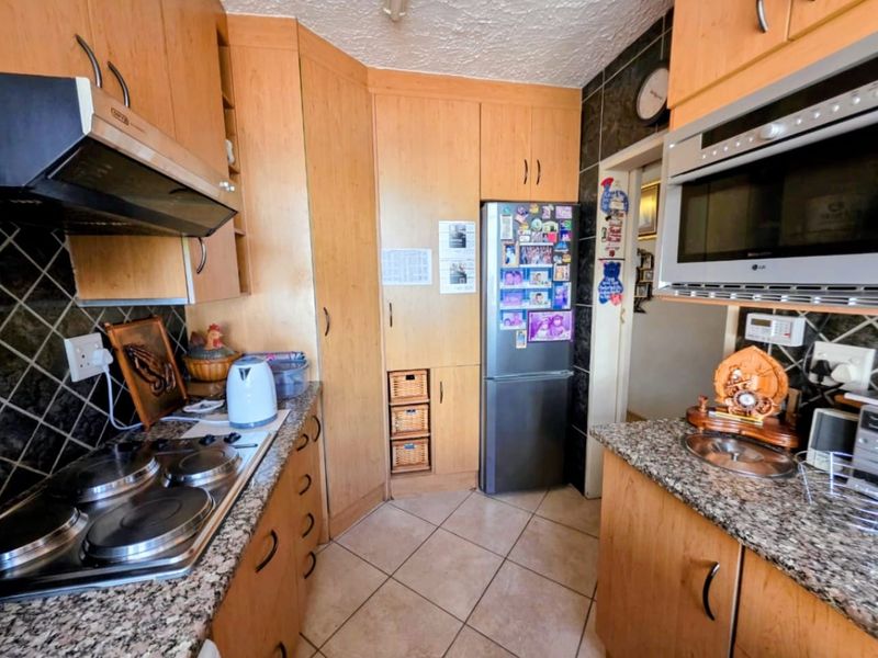 A functional kitchen featuring light wood cabinetry, granite countertops, an electric hob with extractor, and built-in microwave, finished with tiled flooring and backsplash.