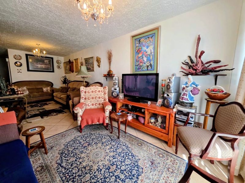 A spacious living room featuring tiled flooring, textured ceilings, and dual crystal chandeliers, offering a comfortable and traditional living environment.