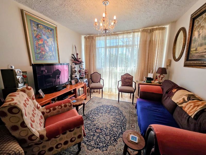 A cozy living room featuring tiled flooring, a central chandelier, and large sliding glass doors that provide natural light.