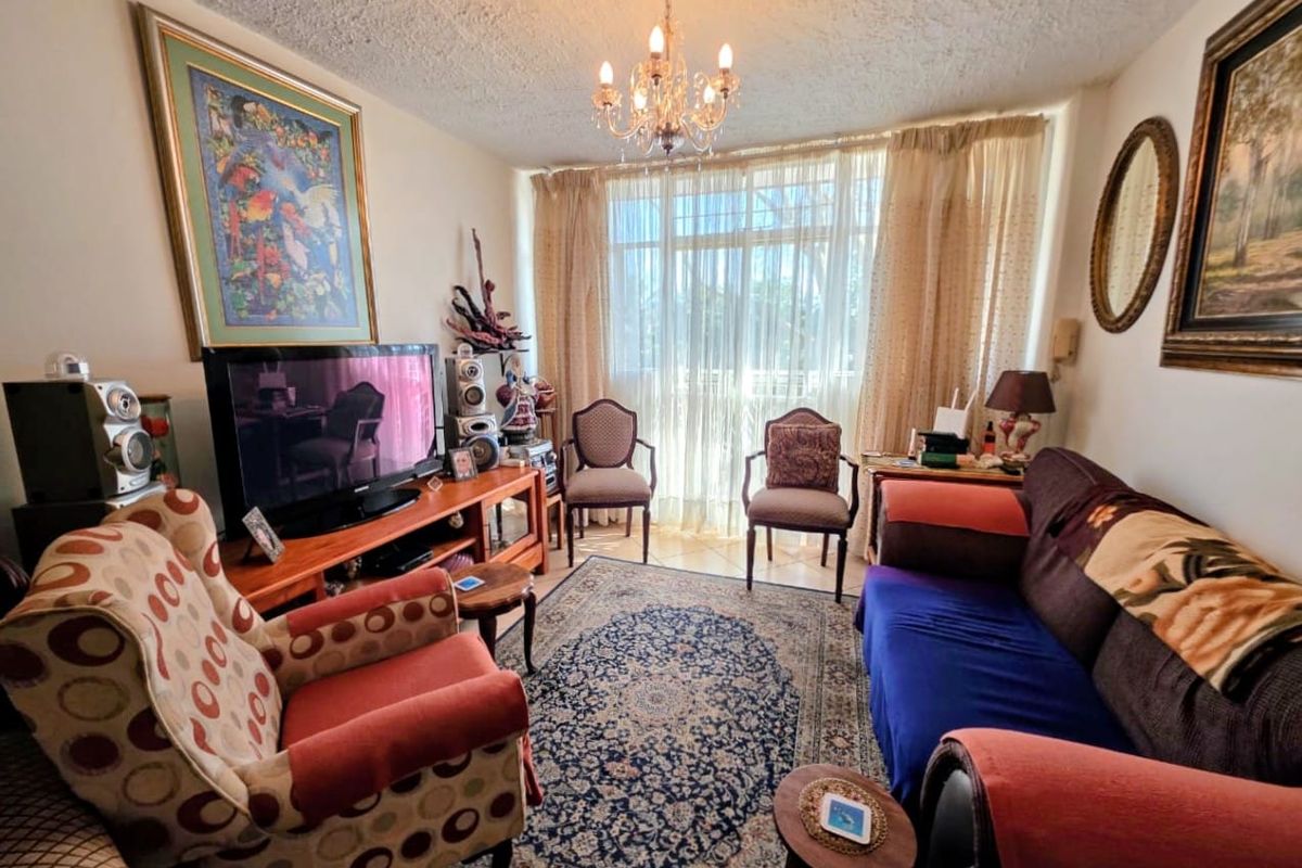 A cozy living room featuring tiled flooring, a central chandelier, and large sliding glass doors that provide natural light.