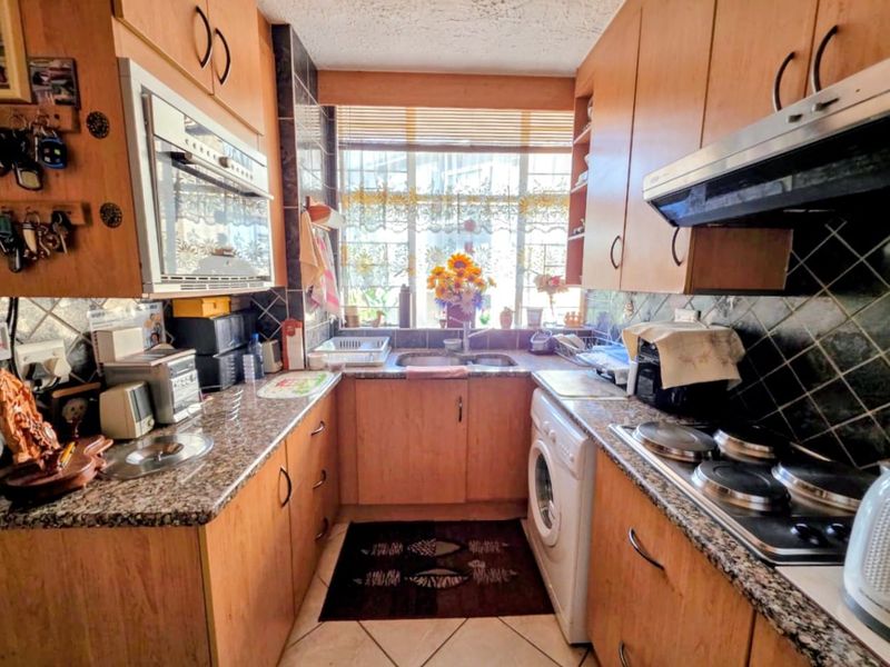 A functional galley-style kitchen featuring wood-finish cabinetry, granite countertops, built-in oven, electric hob, and integrated laundry plumbing under the counter.