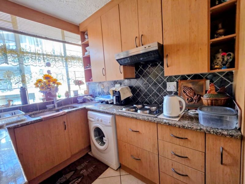 A functional kitchen featuring wood-look laminate cabinetry, granite countertops, a built-in electric hob with extractor fan, and tiled backsplash.
