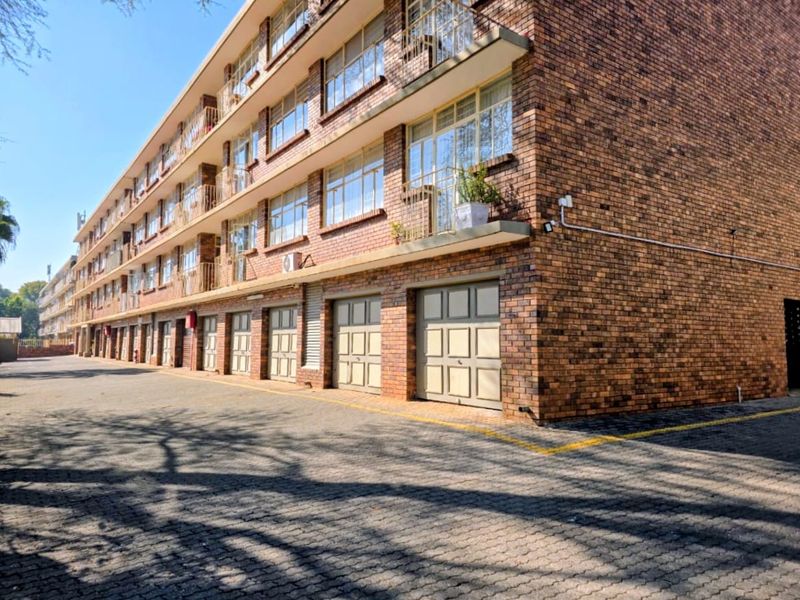 A multi-story apartment building featuring a face brick facade, multiple ground-level garage units, and private balconies for each level.