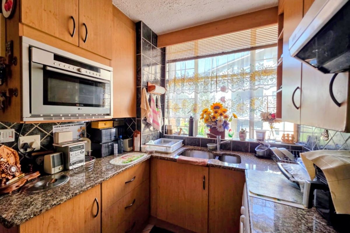 A functional kitchen featuring wood-finish cabinetry, granite countertops, a double sink, and integrated appliances, offering a practical layout with natural light.