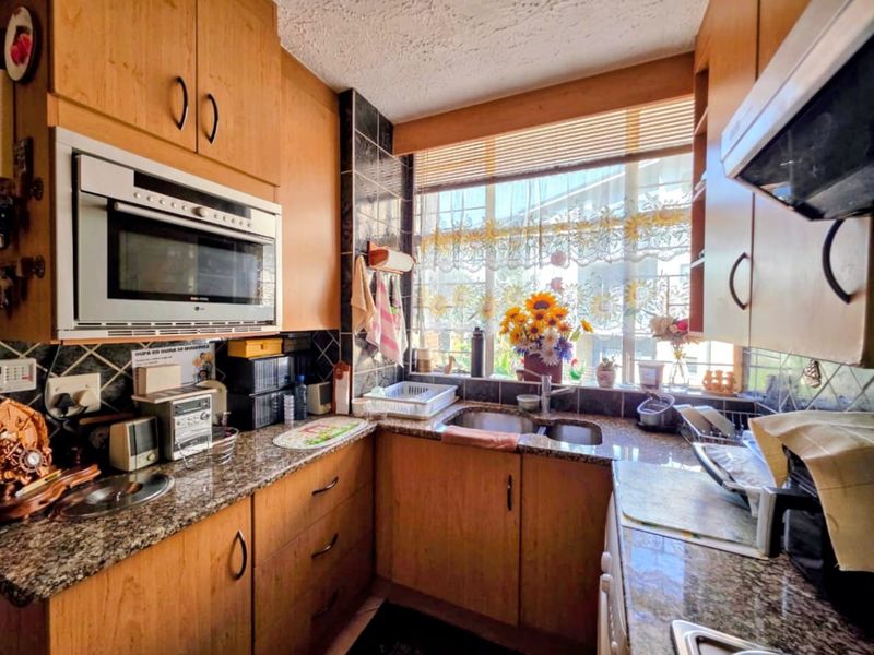 A functional kitchen featuring wood-finish cabinetry, granite countertops, a double sink, and integrated appliances, offering a practical layout with natural light.