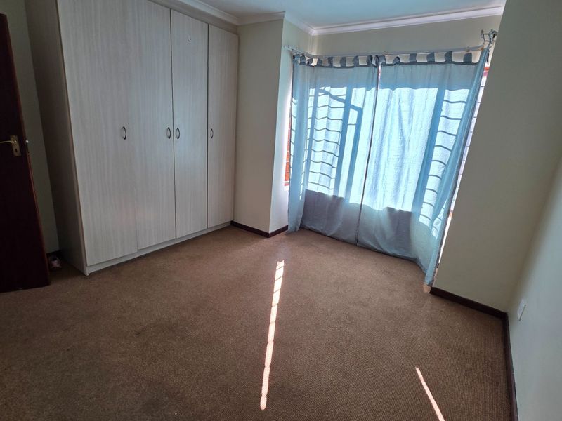 A vacant bedroom featuring neutral built-in cupboards, carpeted flooring, and large windows fitted with security bars.