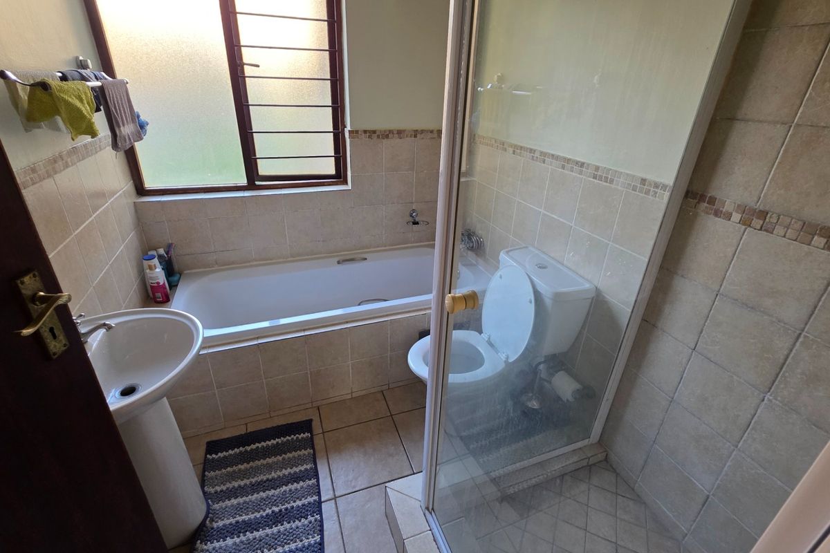 A functional bathroom featuring a pedestal basin, built-in bathtub, separate shower enclosure, and tiled finishes throughout.