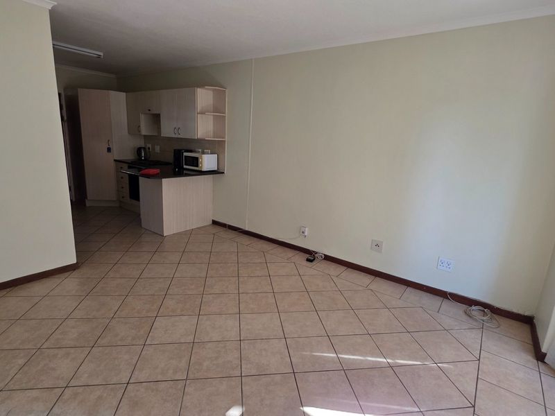 An open-plan living area featuring tiled flooring and a compact, functional kitchen with built-in cabinetry and appliances.