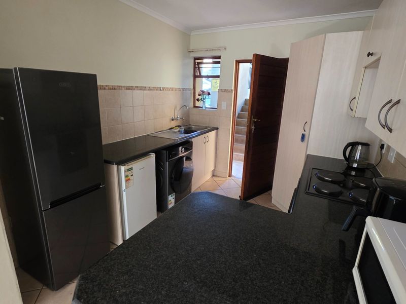 Compact kitchen featuring granite countertops, built-in cabinetry, tiled backsplash, and an integrated electric hob, providing a functional workspace.
