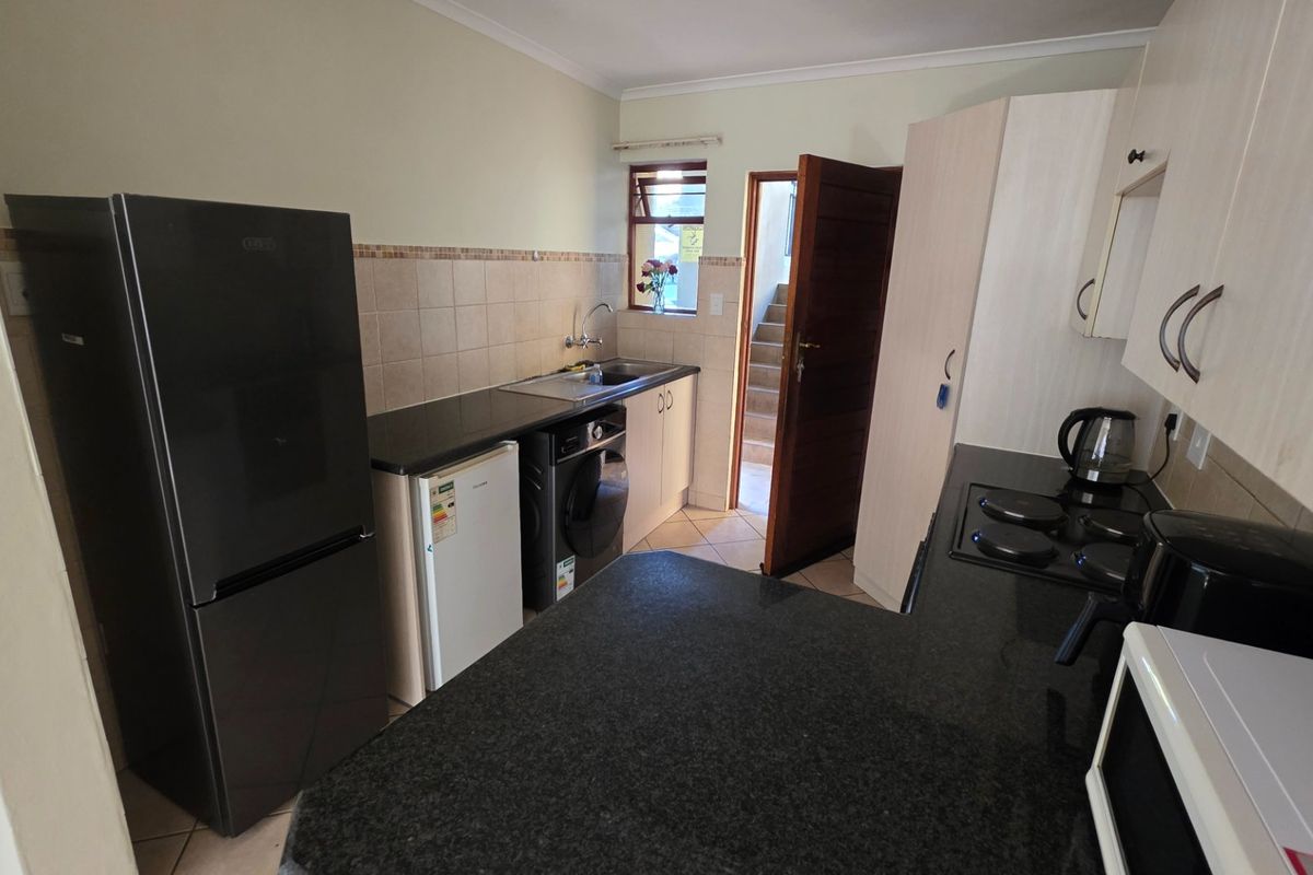 Compact kitchen featuring granite countertops, built-in cabinetry, tiled backsplash, and an integrated electric hob, providing a functional workspace.