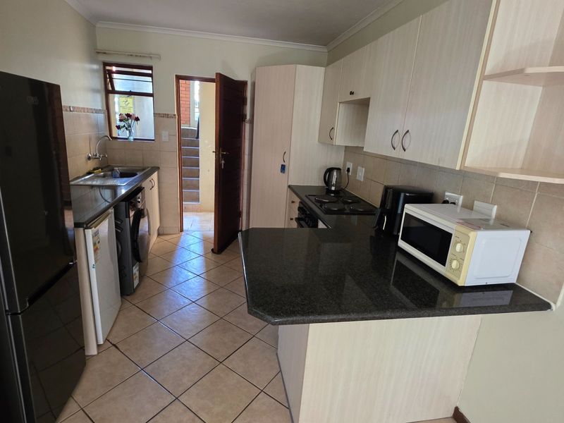 Functional kitchen featuring granite countertops, ample built-in cabinetry, tiled backsplash, and ceramic flooring with direct access to an exterior entrance.