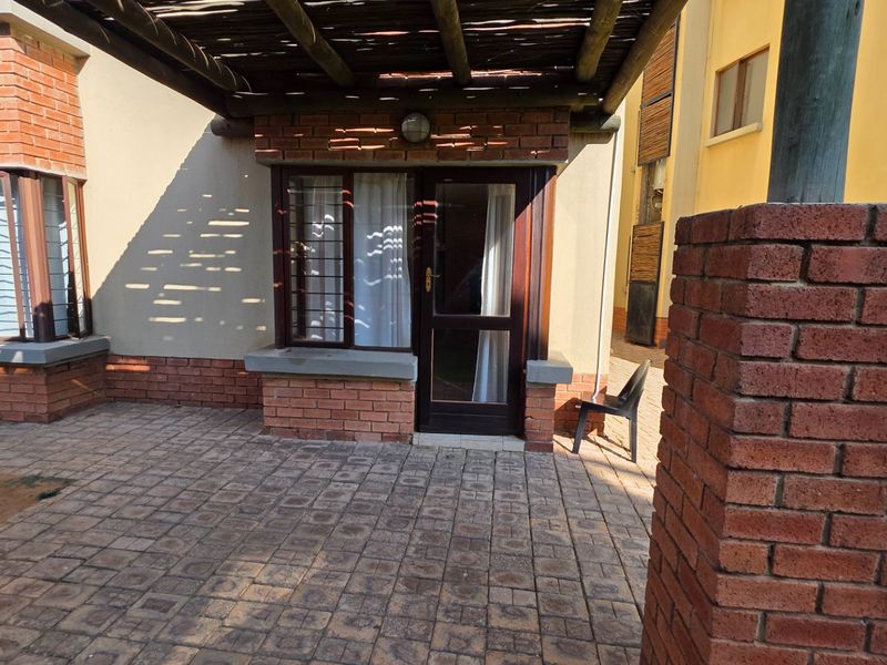 A paved outdoor patio area featuring a timber pergola, brick pillars, and direct access to the apartment through a security door.