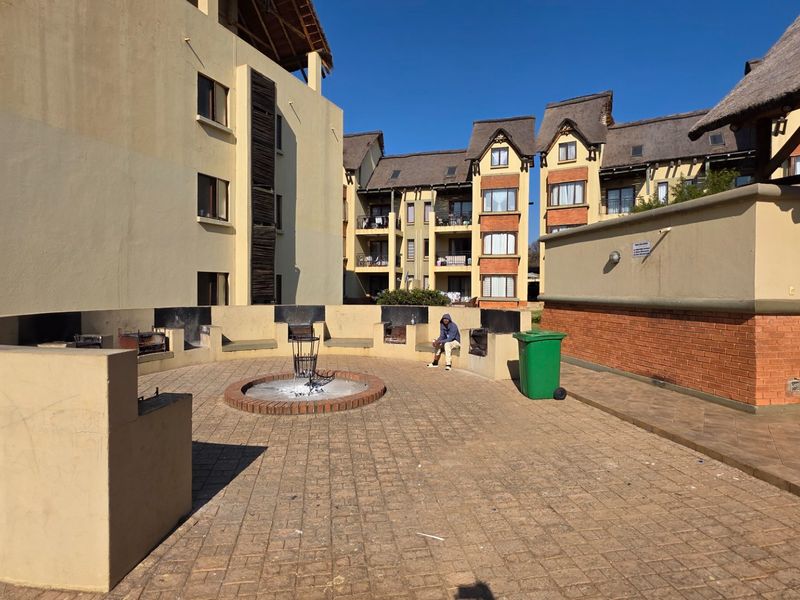 Communal outdoor entertainment area featuring a paved courtyard, built-in braai facilities, and a central fire pit within an apartment complex.