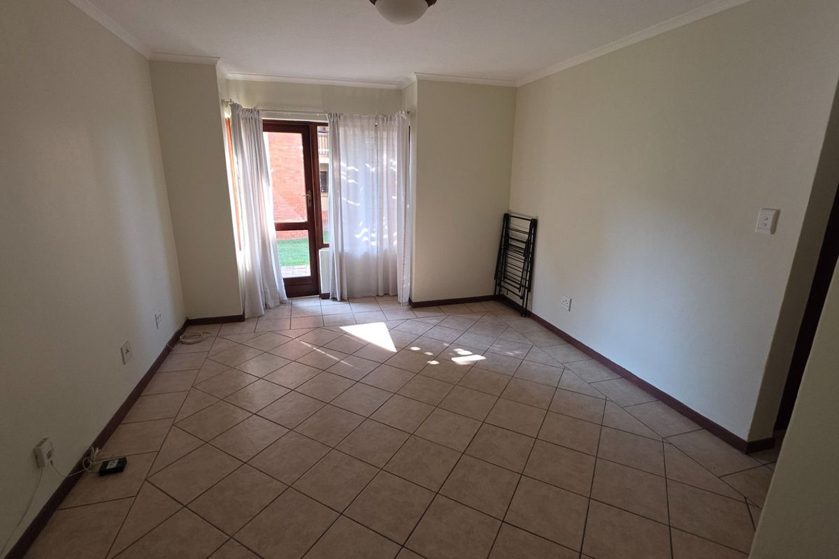 An empty, neutrally painted living room featuring tiled flooring and a glass panel door providing access to the exterior.