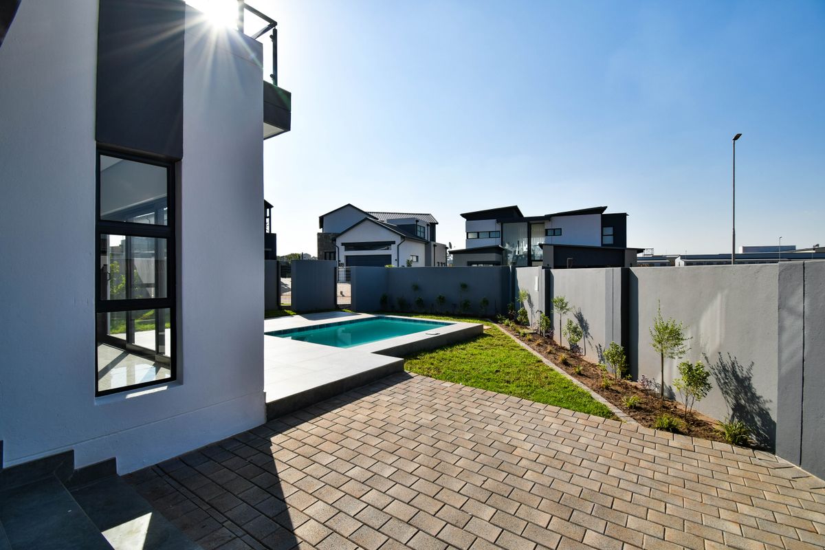 A modern rear exterior featuring a paved patio, a compact swimming pool, and a well-maintained garden enclosed by a solid boundary wall.