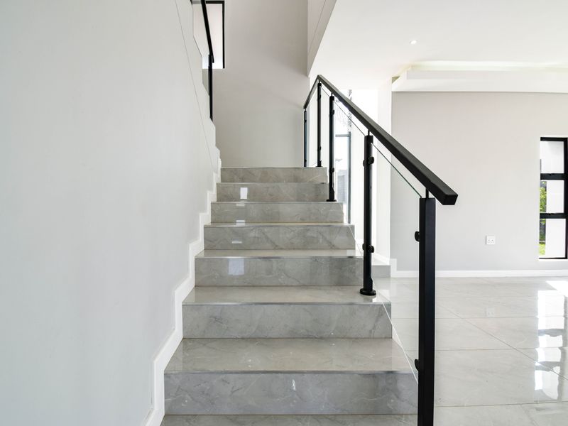 Modern hallway featuring a sleek marble staircase with a contemporary glass and metal balustrade, complemented by polished porcelain floor tiles.