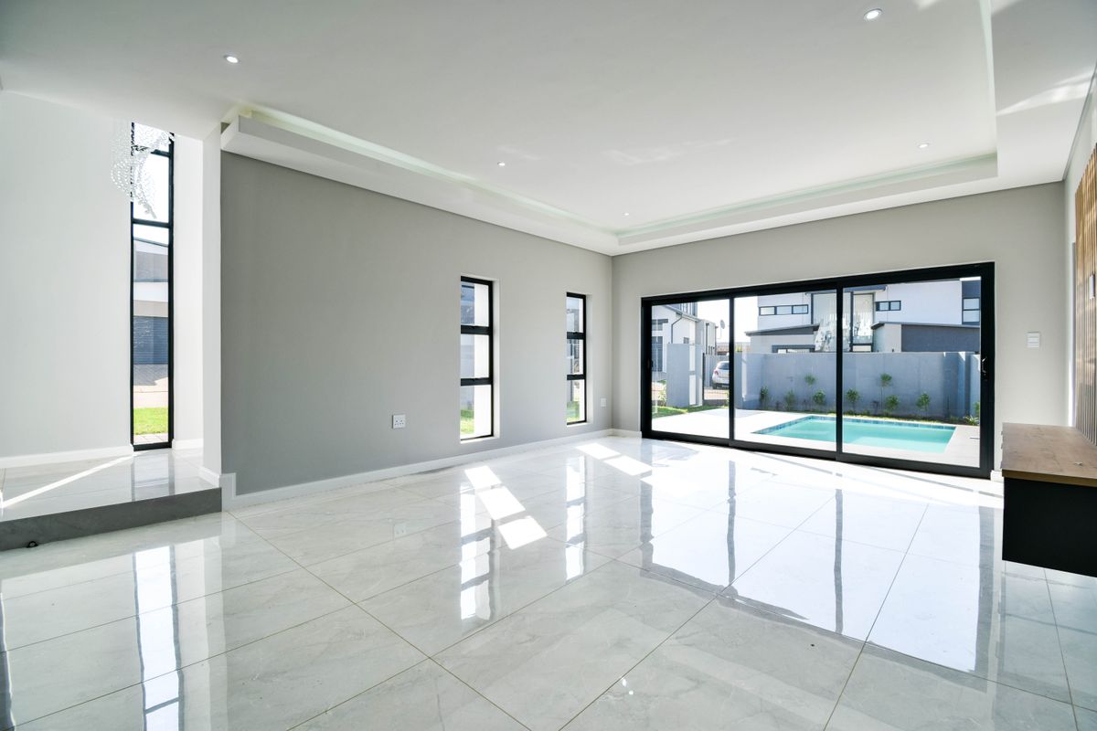 Spacious, modern living area featuring large format floor tiles, recessed ceiling lighting, and expansive sliding glass doors opening to a private pool area.