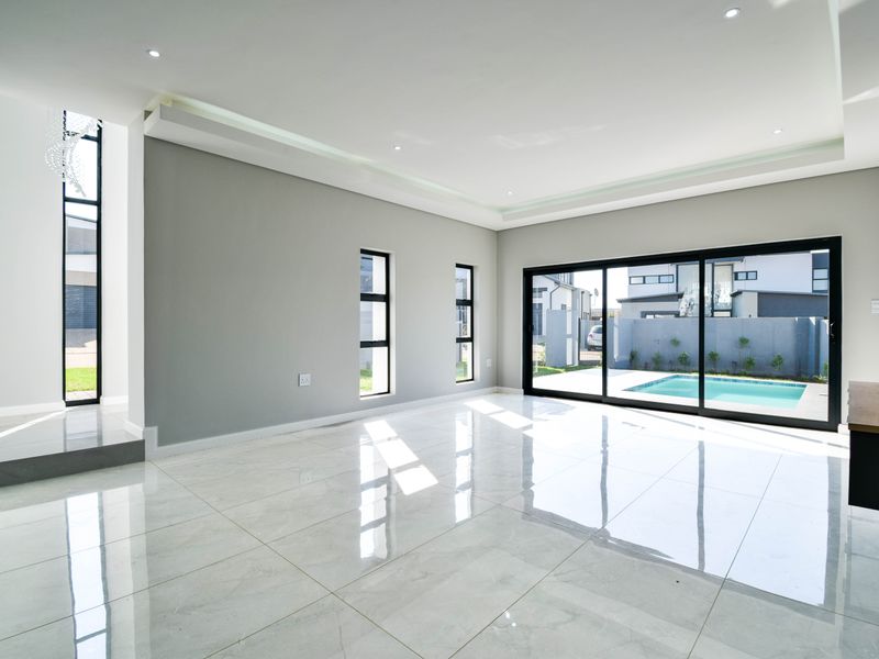 Spacious, modern living area featuring large format floor tiles, recessed ceiling lighting, and expansive sliding glass doors opening to a private pool area.