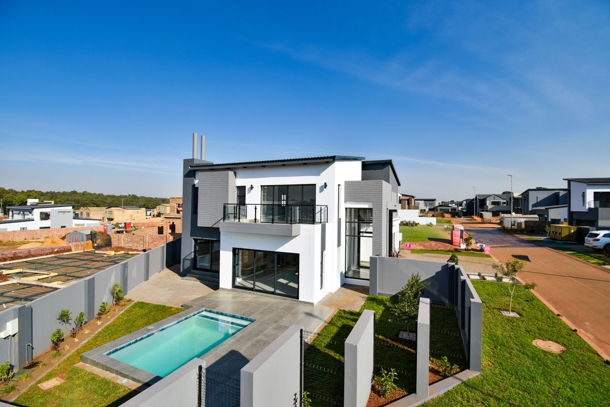 Aerial view of a modern double-story house featuring a swimming pool, paved patio area, and a private balcony with metal balustrades.