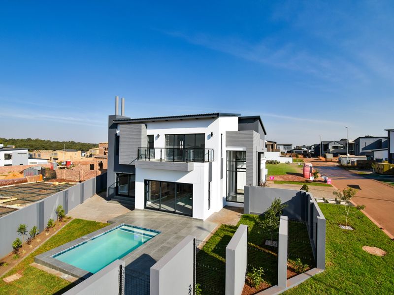 Aerial view of a modern double-story house featuring a swimming pool, paved patio area, and a private balcony with metal balustrades.