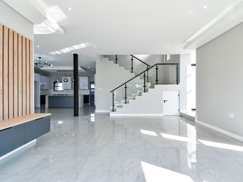 Spacious open-plan living area featuring modern porcelain tiles, a sleek staircase with glass balustrade, and a contemporary kitchen with a central island.