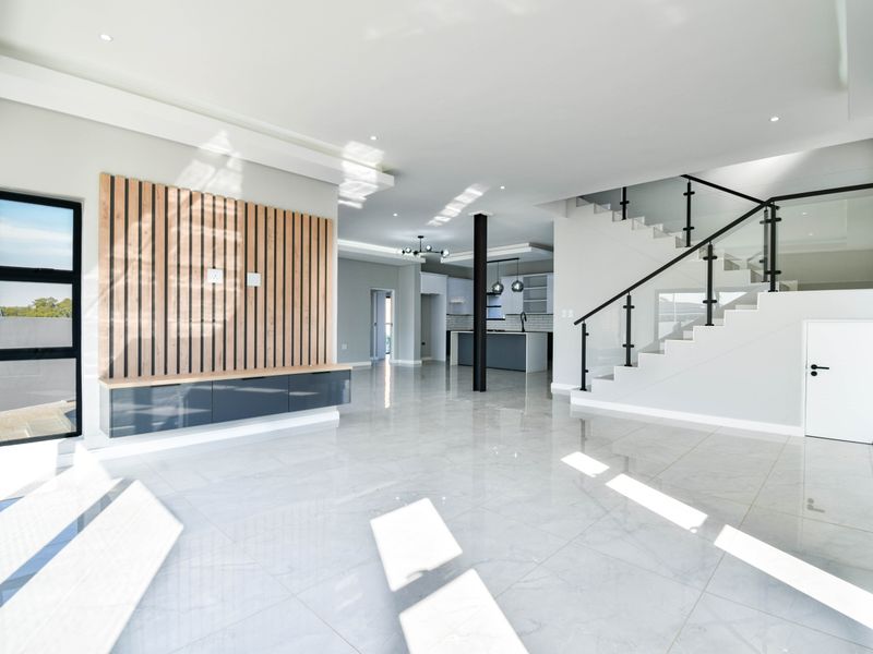 Spacious open-plan living area featuring polished porcelain tiles, a modern timber slat feature wall, and a contemporary staircase with glass balustrades.
