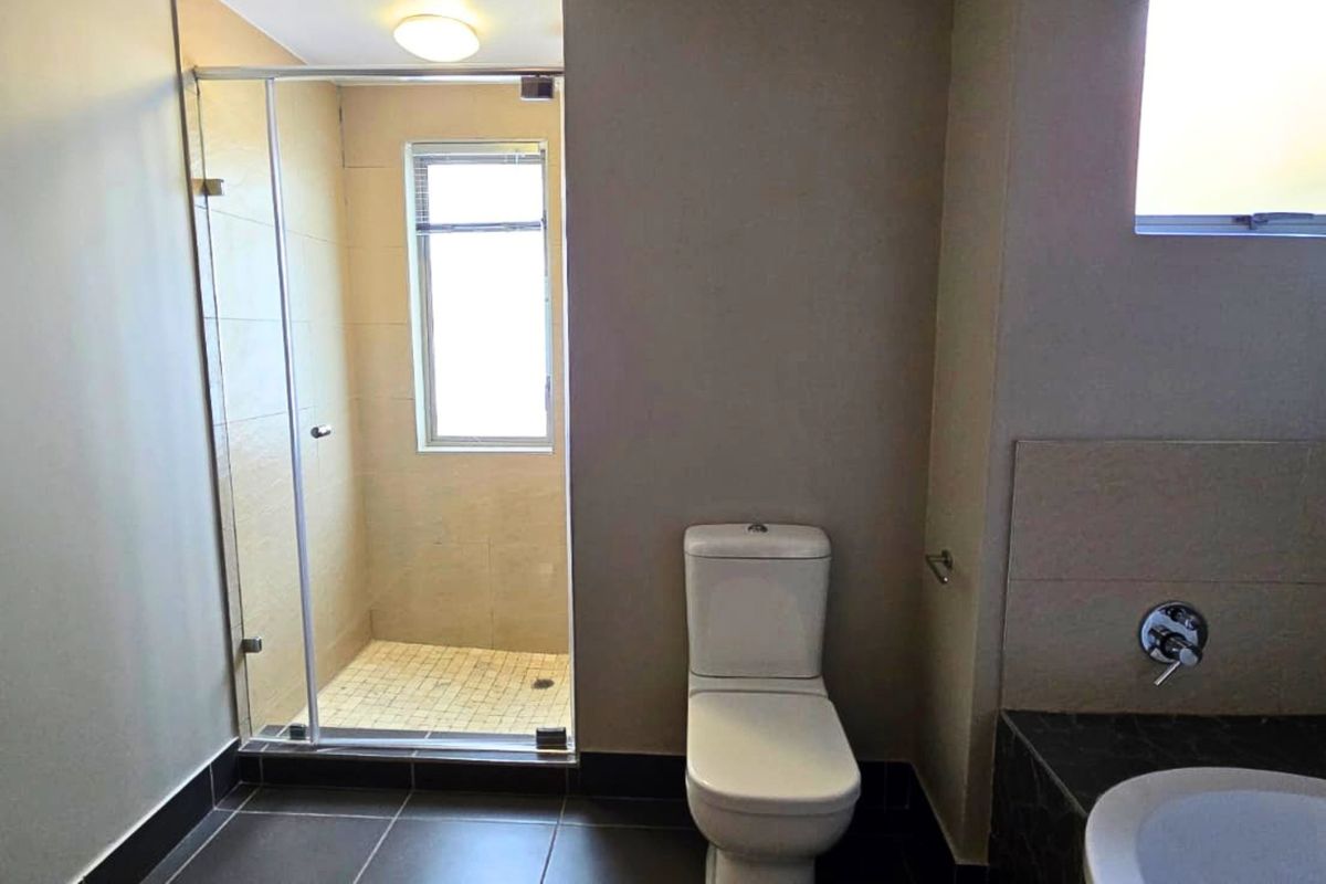 A clean, modern bathroom featuring a glass-enclosed shower, a toilet, and a built-in vanity with neutral tiled finishes throughout.