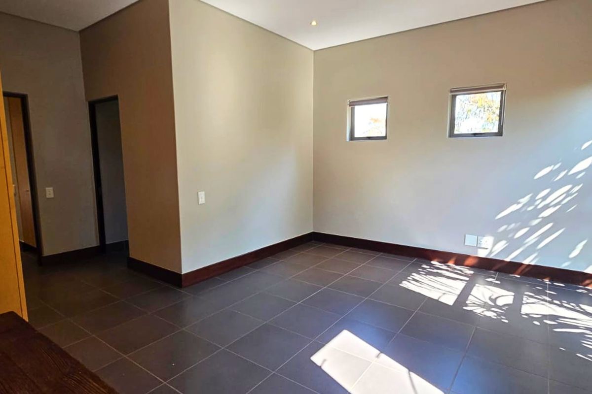 A spacious, empty bedroom featuring neutral walls, dark tiled flooring, built-in cupboards, and large windows that provide ample natural light.