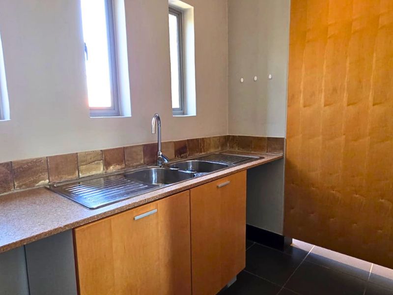 A functional scullery area featuring a stainless steel double sink, laminate cabinetry, and tiled backsplash, providing additional prep and wash-up space.