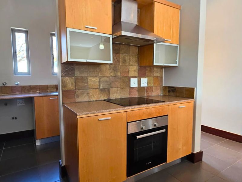A functional kitchen featuring light wood cabinetry, stone tile backsplash, built-in oven and hob, and ample storage space with integrated pantry cupboards.