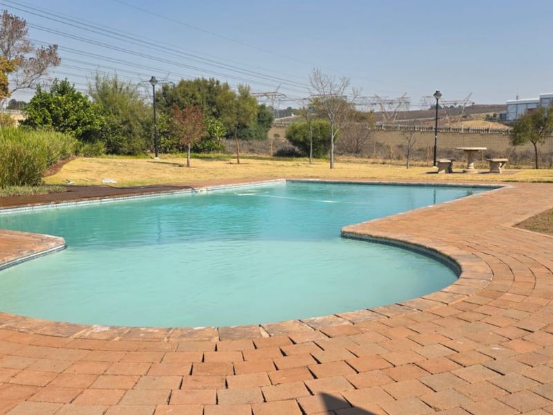 A well-maintained outdoor swimming pool area featuring brick paving and surrounding landscaped garden space.
