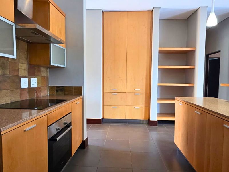 A functional kitchen featuring wooden cabinetry, stone countertops, built-in oven and hob, and ample storage space with a pantry and open shelving.
