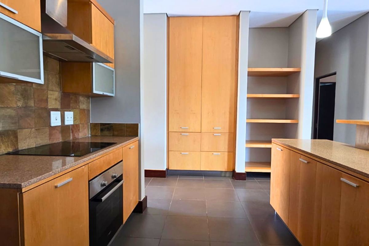 A functional kitchen featuring wooden cabinetry, stone countertops, built-in oven and hob, and ample storage space with a pantry and open shelving.