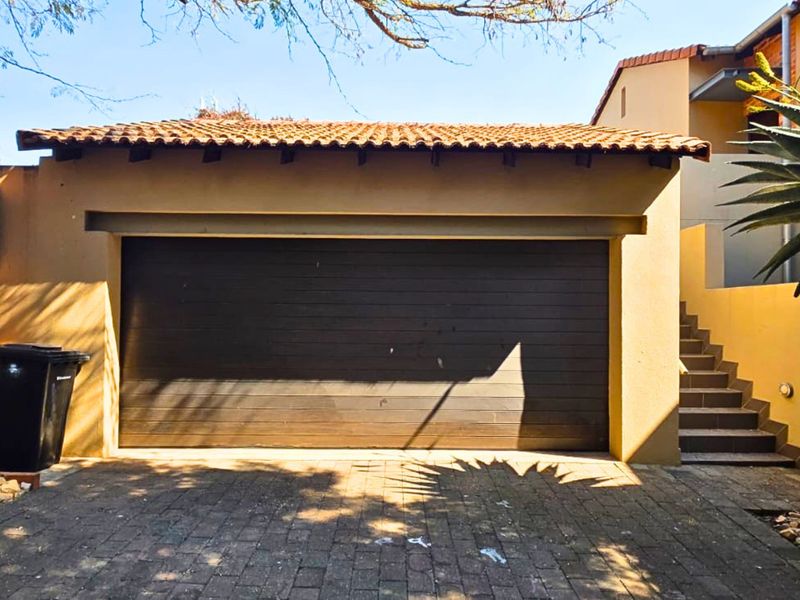 A well-maintained single garage with a sectional door, brick-paved driveway, and an adjacent external staircase leading to the upper level of the townhouse.