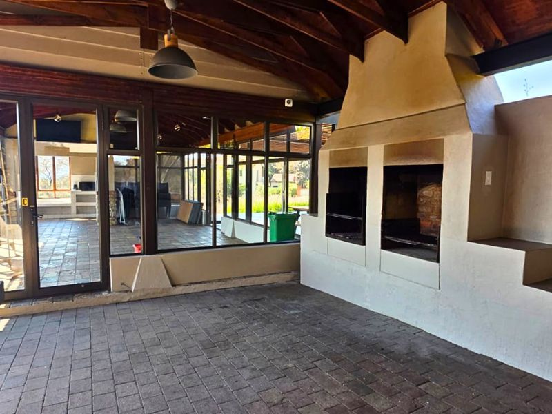 Covered patio area featuring a large built-in braai, exposed timber rafters, and paved flooring, offering a versatile space for outdoor entertaining.