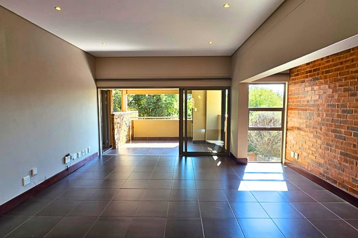 Spacious, empty living area featuring tiled floors, an exposed brick feature wall, and large sliding doors leading to an outdoor balcony.