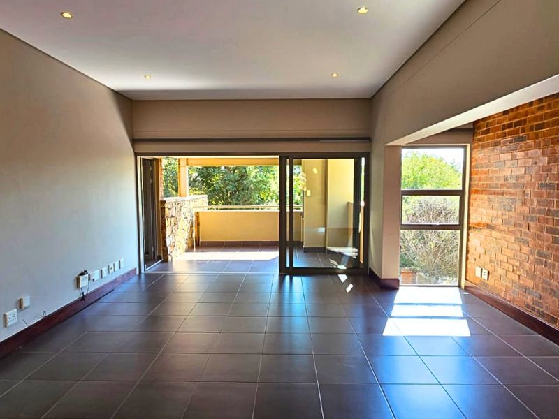 Spacious, empty living area featuring tiled floors, an exposed brick feature wall, and large sliding doors leading to an outdoor balcony.