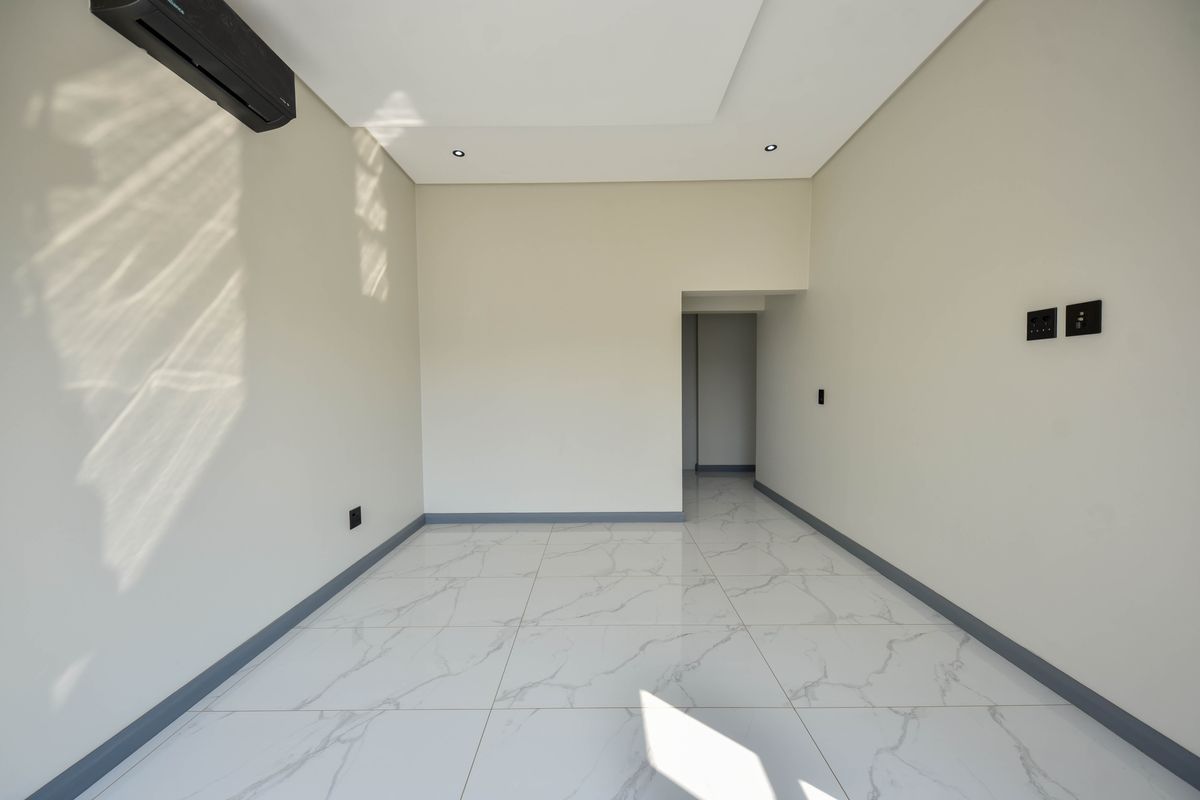 A bright, empty living area featuring modern marble-look floor tiles, recessed ceiling lighting, and a wall-mounted air conditioning unit.