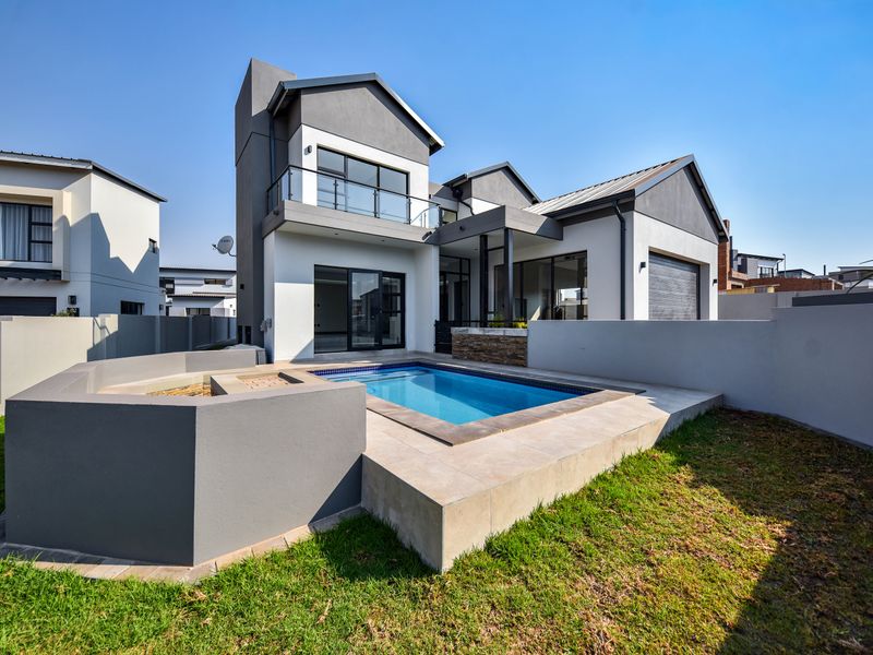 Modern double-story residence featuring a rear swimming pool, tiled patio area, and a balcony overlooking the landscaped garden.