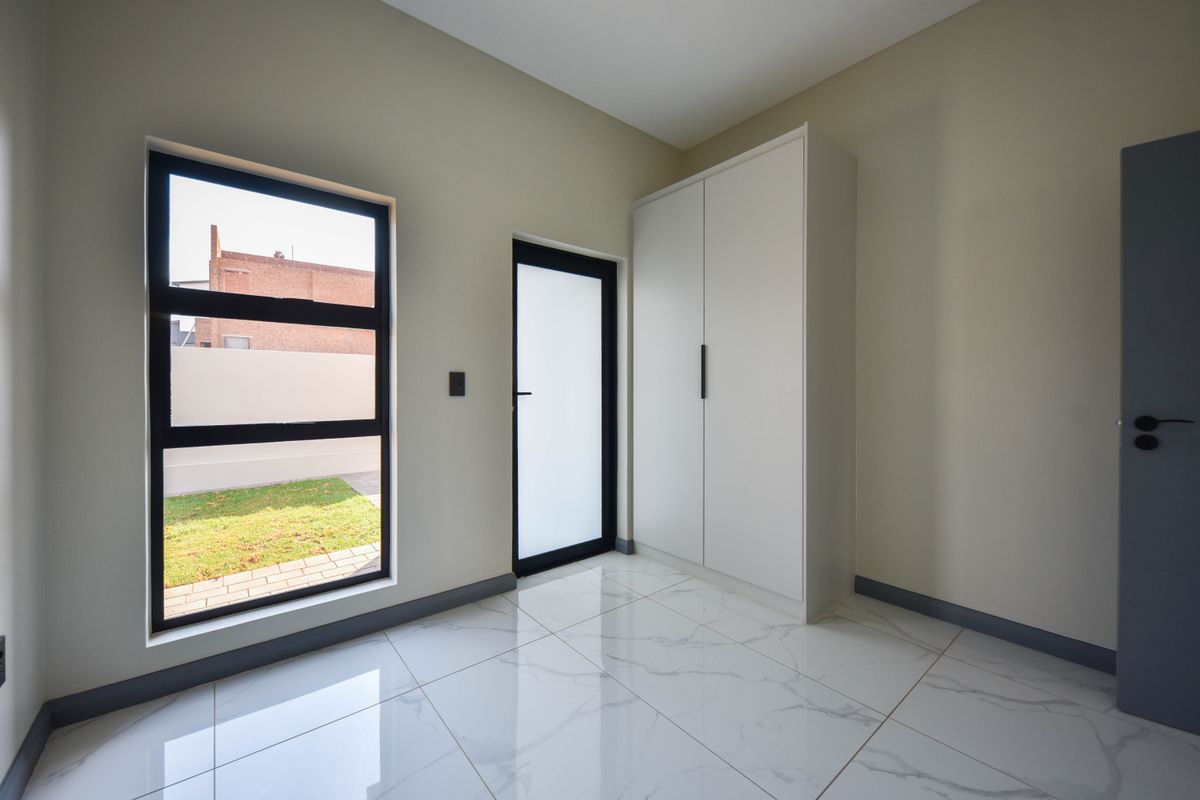 A bright, modern bedroom featuring sleek marble-look tiled flooring, a built-in wardrobe, and a frosted glass door leading to the exterior.