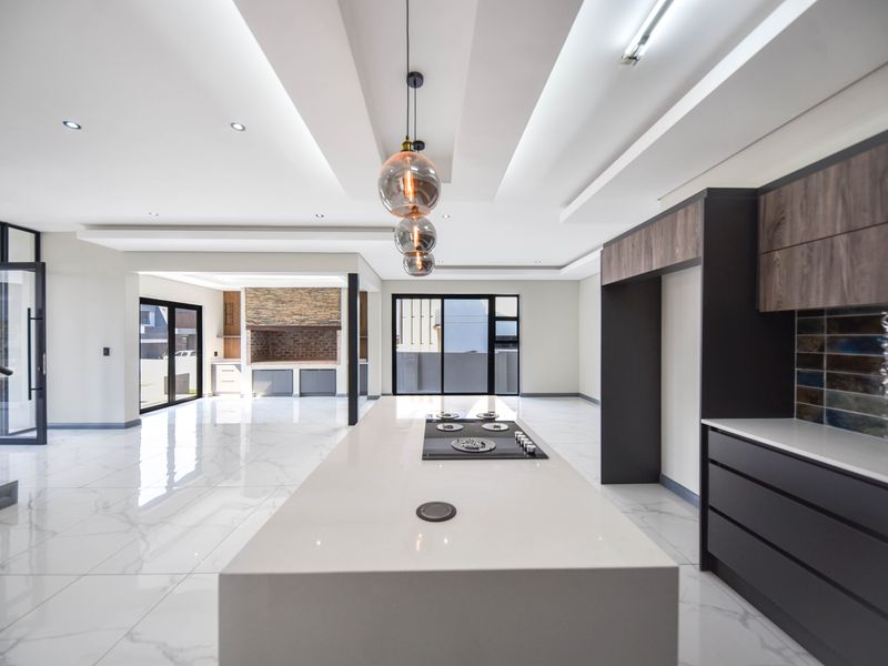 Spacious open-plan living area featuring a modern kitchen island with integrated hob, sleek cabinetry, tiled floors, and a built-in indoor braai area.
