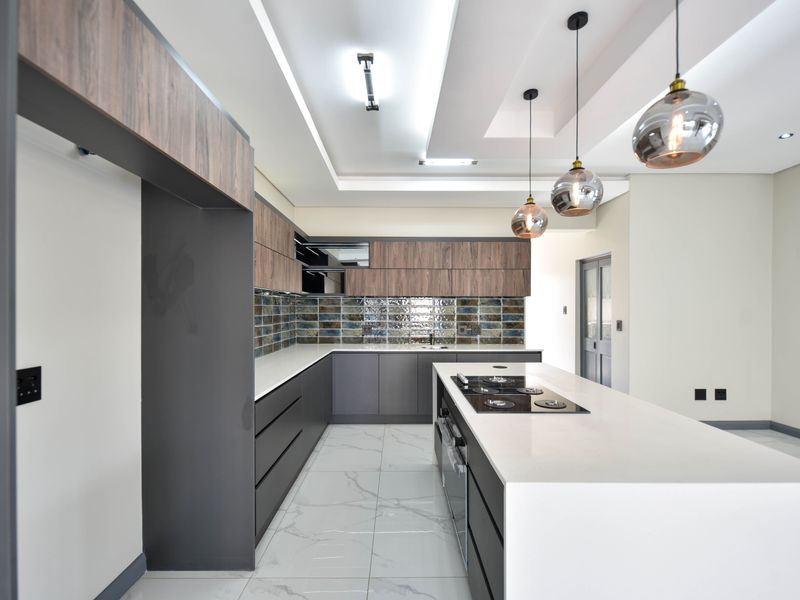 Modern kitchen featuring a large island with built-in hob, sleek cabinetry, stone countertops, and stylish pendant lighting in a bright, open space.