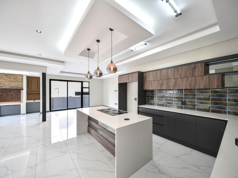 Modern open-plan kitchen featuring a central island with built-in hob, sleek cabinetry, stone countertops, and stylish tiled backsplash with recessed ceiling lighting.
