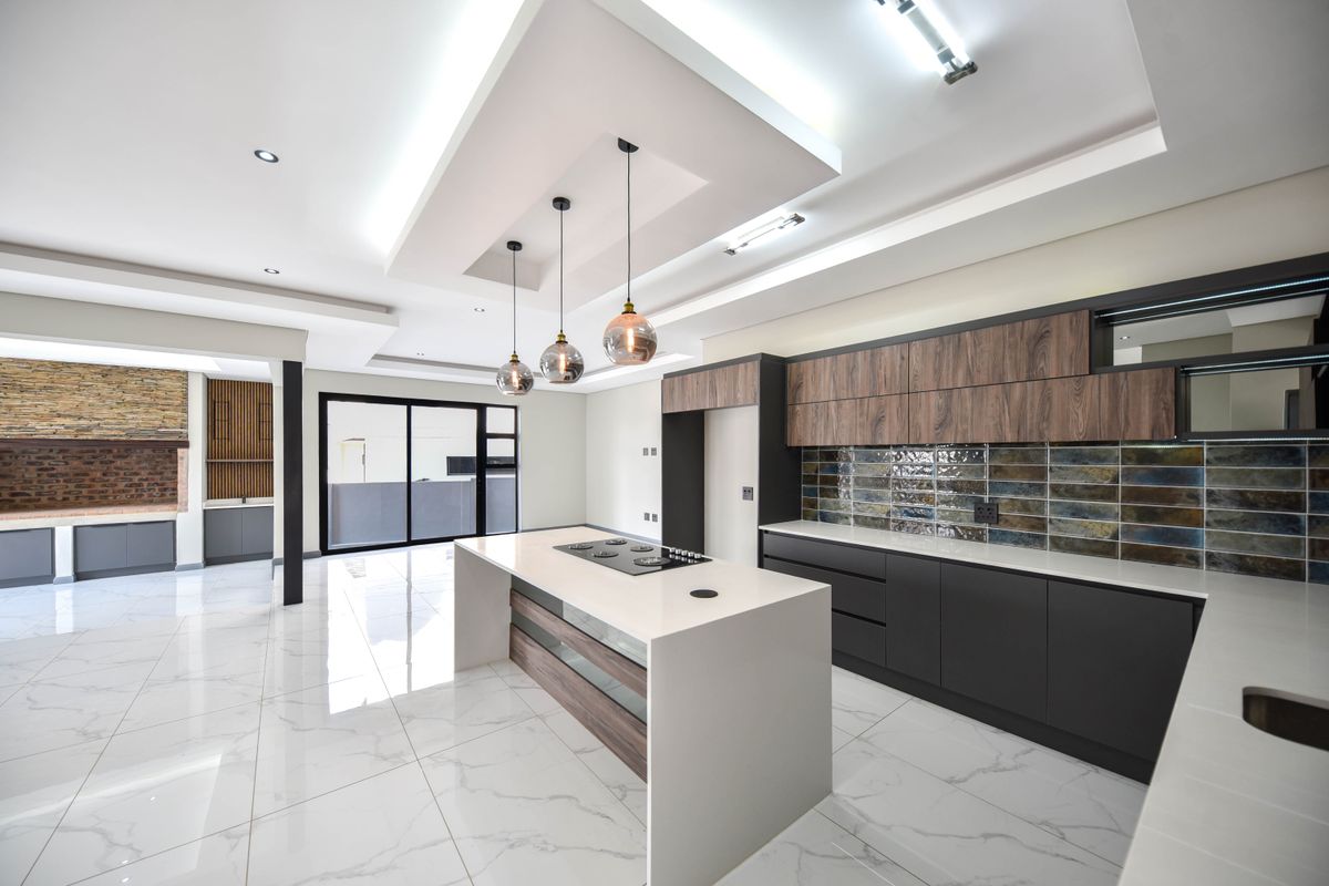 Modern open-plan kitchen featuring a central island with built-in hob, sleek cabinetry, stone countertops, and stylish tiled backsplash with recessed ceiling lighting.