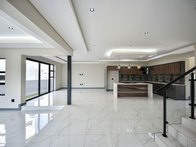 Spacious open-plan living and kitchen area featuring high-end marble-look floor tiles, modern cabinetry, and a sleek glass balustrade staircase.
