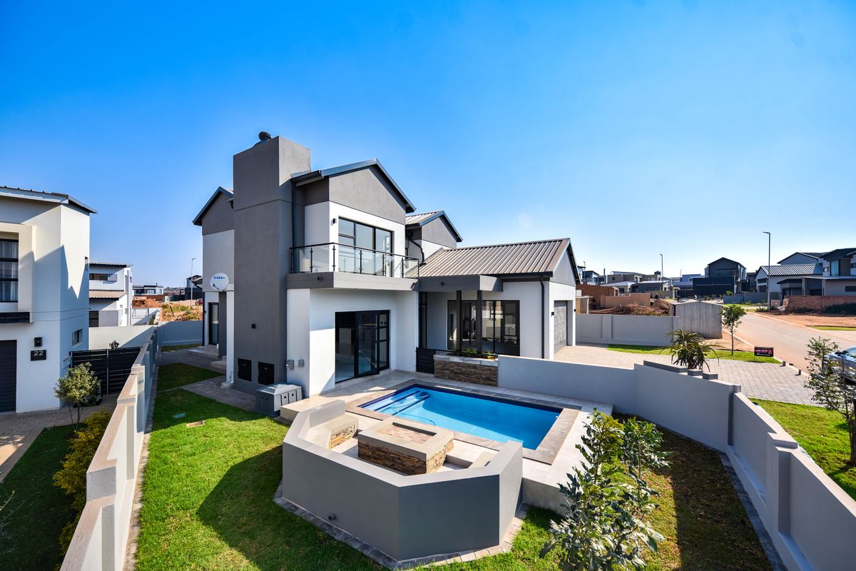 Rear view of a modern double-story house featuring a swimming pool, built-in fire pit, paved patio area, and a balcony with glass balustrades.