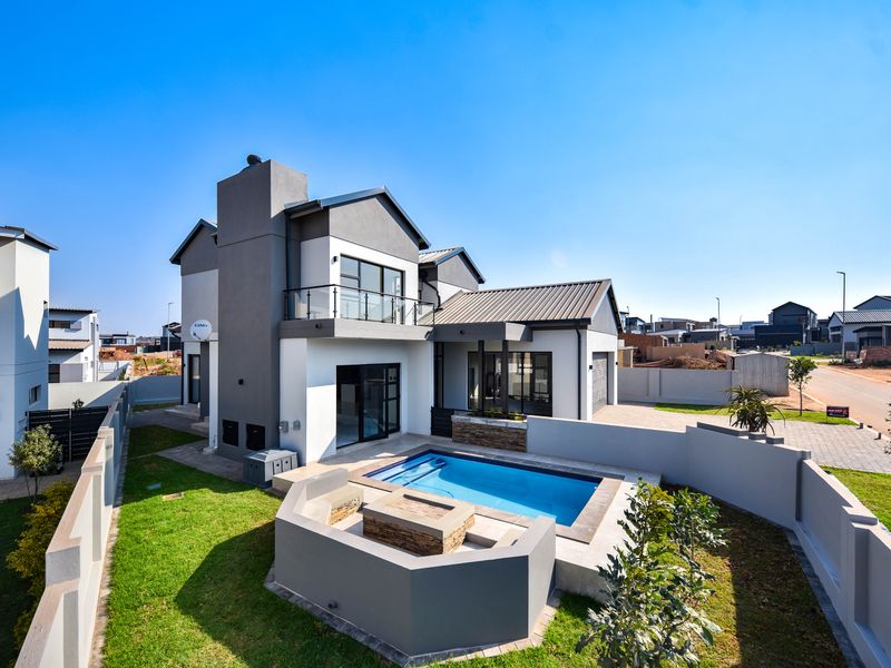 Rear view of a modern double-story house featuring a swimming pool, built-in fire pit, paved patio area, and a balcony with glass balustrades.
