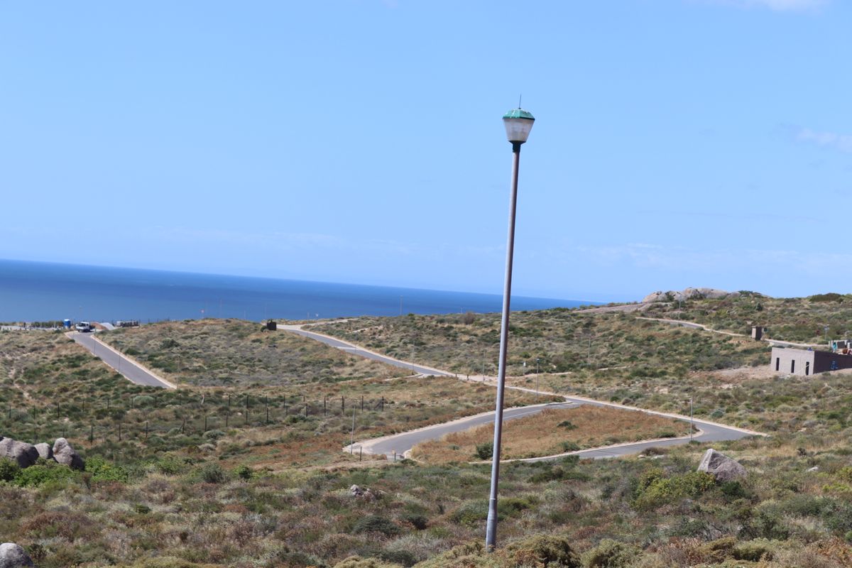 An elevated view of a vacant residential development site featuring paved roads, street lighting, and coastal landscape views.